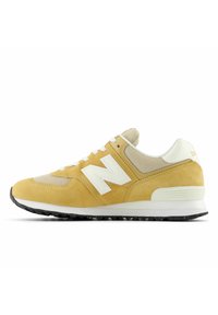 Zapatillas amarillas de ante con paneles de malla, acentos blancos y una suela negra texturizada. Presentan cordones y un destacado logo 'N' en el lateral.