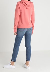 Růžová mikina s volným střihem a kapucí, spárovaná se světle modrými slim-fit džíny. Bílé tenisky s růžovými akcenty dotvářejí outfit.