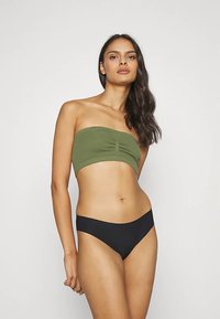 Top bandeau fără bretele, verde măsliniu, cu detalii drapate, asortat cu slip negru de bikini, evidențiind un material neted și un design ajustat.