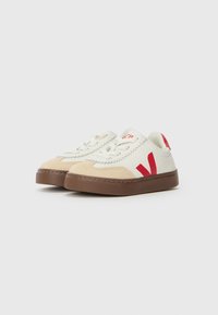Hvite lerrets sneakers med røde detaljer, beige semsket skotupp og brun gummisåle. Har sydd detaljer og snøring.