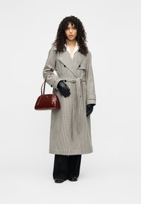 Διπλής σειράς καρό παλτό τύπου trench σε ανοιχτό γκρι και μαύρο, με ταιριαστή ζώνη. Μαύρα δερμάτινα γάντια και μια μικρή μπορντό τσάντα χειρός. Μαύρο παντελόνι.