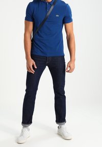 Blue polo shirt with short sleeves, dark denim jeans, and white sneakers. Accessories include a small black shoulder bag.