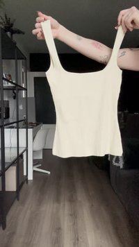 Kremo spalvos juostelėmis tank topas su plonomis petnešėlėmis, turintis kvadratinį iškirpimą ir prigludusią formą. Medžiaga atrodo minkšta ir tekstūruota.