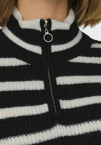 Zwart-wit gestreepte gebreide pullover met een hoge kraag en ritssluiting. De stof heeft een zachte textuur en een opvallend ribbelpatroon.