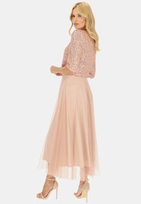 Różowa spódnica z tiulu w połączeniu z cekinową bluzką z krótkim rękawem. Strój charakteryzuje się zwiewnym krojem, miękką fakturą oraz neutralnymi szpilkami.