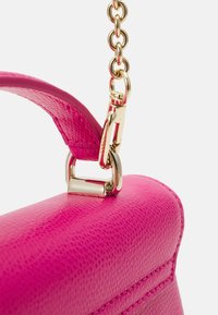 Roh růžové kožené kabelky s texturovaným povrchem, vybavený zlatým kovovým řetízkovým popruhem a zapínacím detailem pro připevnění.