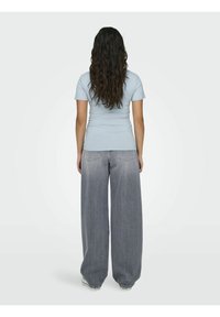 Lys blå tettsittende T-skjorte kombinert med høy midje, vide grå jeans. Jeansene har en gradvis falming og klassiske baklommer.