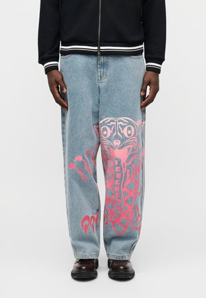 Vaaleansiniset farkut, joissa on suuri vaaleanpunainen tiikerikuva ja sana "ICECREAM" oikeassa etujalassa, yhdistetty mustiin kenkiin.