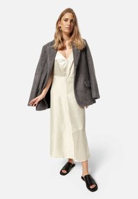 Grau strukturierte Umhangjacke über einem cremefarbenen Slipkleid mit glänzender Oberfläche; schwarze Slipper-Sandalen; schlichtes Design, keine sichtbaren Muster oder Akzente.