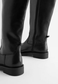 Stivali neri in pelle al ginocchio con finitura liscia, suola robusta, dettagli minimi e una zip laterale per una facile indossabilità.