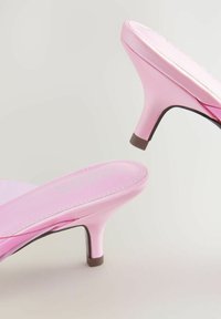 Rozā satīna augstpapēžu sandales ar elegantu dizainu, ar plānu papēdi un mīkstinātu zoli, uz kuras redzams logo.