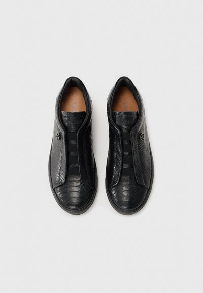 Adidași negri texturați, tip slip-on, cu benzi elastice și emblemă logo pe lateral, văzuți dintr-o perspectivă de sus pe un fundal alb simplu.
