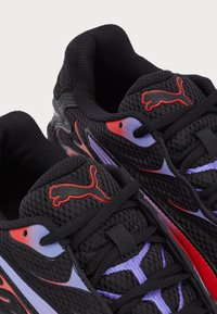 Black mesh running shoes with red and purple accents, featuring textured surfaces, thin laces, and a prominent Puma logo on the tongue.