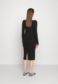 Μαύρο πλεκτό φόρεμα με ριχτές ραφές και μακριά μανίκια, μήκους μέχρι το γόνατο. Διαθέτει σχισμή στην πλάτη για ευκολία κινήσεων. Συνδυάζεται με μαύρα και λευκά ριγέ φλατ παπούτσια.