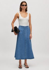 Denim rok met een uitlopende silhouet, lichtblauwe kleur en een voorkantnaad. Gepaard met een witte tanktop en een zwarte clutch, gedragen met sandaaltjes.
