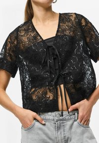 Czarny koronkowy krótki top z kwiatowym wzorem, krótkimi rękawami i cekinami. Posiada głęboki dekolt w kształcie litery V oraz zapięcie na wstążkę z przodu.