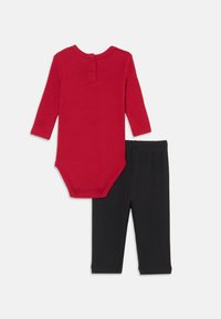 Bodysuit rouge à manches longues avec un col rond et une fermeture à pression au dos, associé à des leggings noirs. Les deux articles sont fabriqués en tissu doux et extensible.