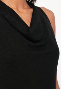 Μαύρο αμάνικο τοπ με λαιμόκοψη καμπάνα, κατασκευασμένο από λείο ύφασμα. Διαθέτει εφαρμογή που αγκαλιάζει το σώμα και διακριτική γυαλάδα.