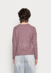 Lila stickad tröja med långa ärmar, ribbad sluttning och texturerat mönster. Matchad med ljusgrå löst sittande byxor, utan synliga metalldelar eller accenter.