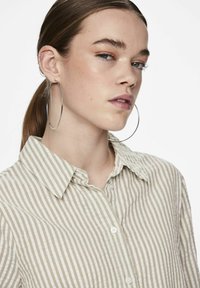 Camicia a righe in tessuto beige e bianco, con colletto e maniche lunghe. Orecchini a cerchio grandi in argento completano il look.