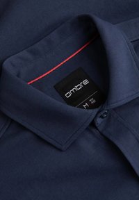 Marinemarine blauwe polo met een kraag, voorzien van een contrasterende rode accent in de kraag en een zwart label met merknaam en maat.