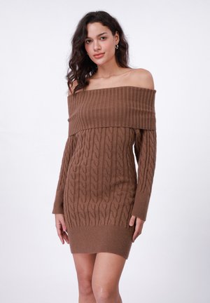 Haljina od smeđeg pletenog materijala s off-shoulder izrezom, koja prikazuje kabelne uzorke, dugačke rukave i rebrastu teksturu. Haljina je do koljena, s uskim i udobnim dizajnom.