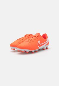 Nike fotballsko i lys orange med teksturert overdel, hvite detaljer og formede knotter for grep. Har lisser og støttende hæl.
