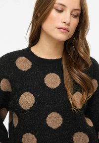 Mustast pehmest materjalist kampsun, millel on suured beežid ringid. Ümar kaelus ja tekstuuriga viimistlus nähtavate kiududega.