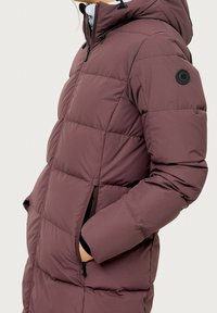 Bordeauxfarbene Pufferjacke mit Kapuze, ausgestattet mit einem Reißverschluss, Seitentaschen und einem runden Logo am Oberarm. Texturiertes, gesteppte Design.