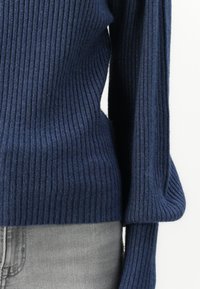 Navy blue ribbed sweater with long sleeves, featuring a textured knit pattern and a fitted design at the waist, paired with gray denim.