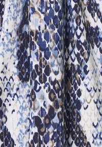 Tissu imprimé animal bleu, noir et beige avec des accents de fils métalliques dorés verticaux et une surface tissée texturée.
