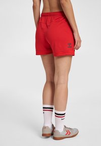 Röda sportshorts med resårband i midjan, med en logotyp på sidan. Kombinerat med vita strumpor med svarta och röda ränder samt grå sneakers.