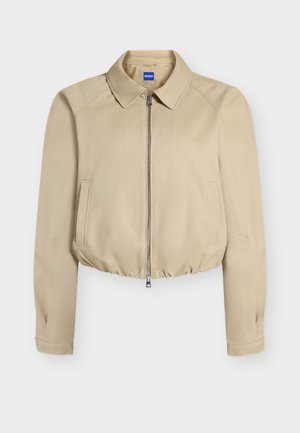 Veste courte beige avec fermeture éclair à l'avant, col pointu, manches longues, poches latérales et ourlet élastiqué, étiquetée "Hugo" à l'intérieur du col.