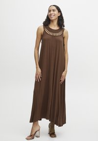 Robe maxi sans manches marron avec un design de col découpé tissé. Fabriquée en tissu doux, elle présente une silhouette ample et fluide. Sandales à talons blocs transparents.