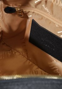 Interno di una borsa nera con una fodera beige liscia, dotato di una tasca con zip e un'etichetta in tessuto nero testurizzato sul lato.