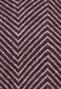 Knitted fabric with dark purple and white zigzag chevron pattern, texture showing soft, fuzzy yarn fibers.