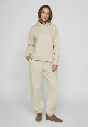 Pantalones de chándal beige y sudadera con capucha a juego. Textura suave, corte relajado, bolsillo frontal en la sudadera, tobillos ajustados en los pantalones.