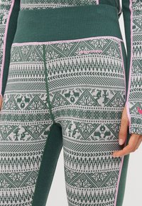 Green patterned leggings featuring a textured knit material, ribbed waistband, and pink accents. Designs include geometric shapes and animal motifs.