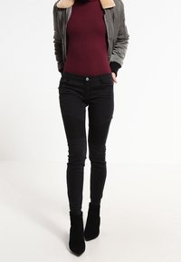 Černé skinny džíny s texturovanými kolenními panely, vysokým pasem a středně vysokým střihem, kombinované s přiléhavým burgundským topem a olivovým bomberem.