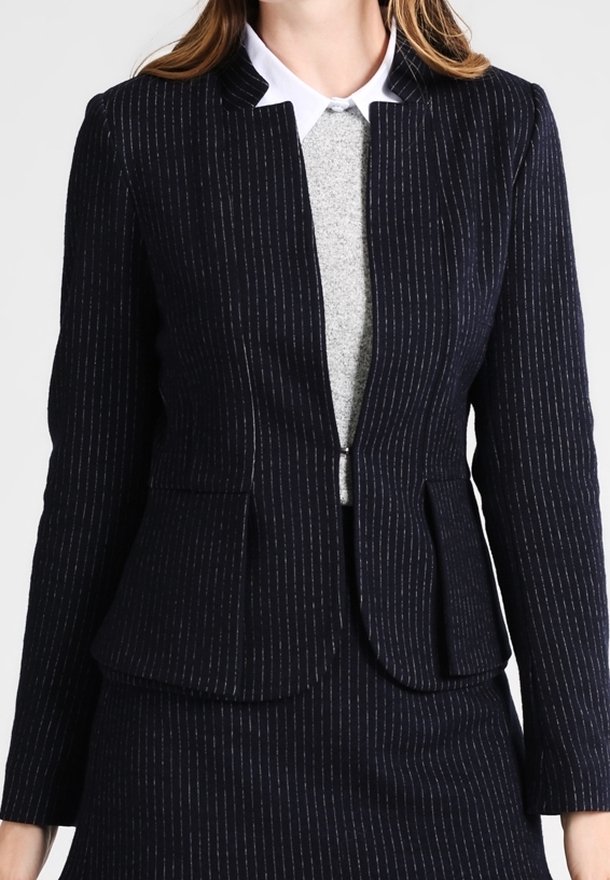 Tummansininen pinstripe-kuvioitu bleiseri, joka on valmistettu teksturoidusta kankaasta ja jossa on istuva leikkaus, ilman kauluksia ja kaksi etutaskua. Päällä harmaa paita.