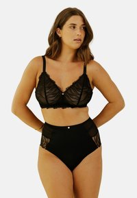 Soutien-gorge en dentelle noire avec un bord festonné, des panneaux transparents et un bouton décoratif central, associé à une culotte noire taille haute ornée d'accents en dentelle.