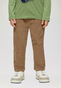Bruine corduroy broek met smalle ribbels, rechte snit en elastische taille, gecombineerd met chunky witte sneakers met grijze accenten.