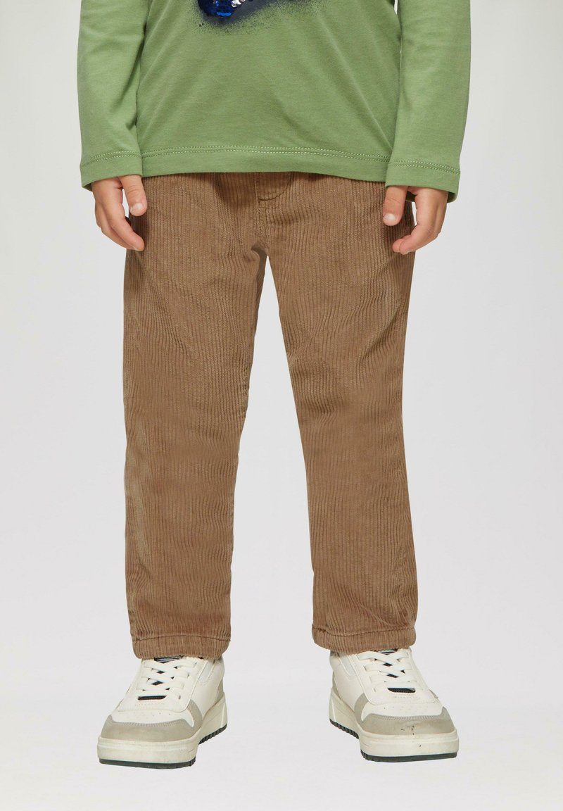 Bruine corduroy broek met smalle ribbels, rechte snit en elastische taille, gecombineerd met chunky witte sneakers met grijze accenten.