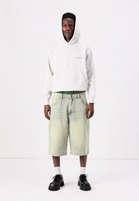 Lys grå hettegenser med frontlomme, kombinert med lyse denimshorts. Svarte snøresko, hvite sokker og grønn rutete livline.