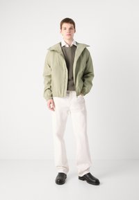 Light green zip-up jacket with a hood, worn over a dark gray sweater. Paired with white pants and black ankle boots. Minimalist design.