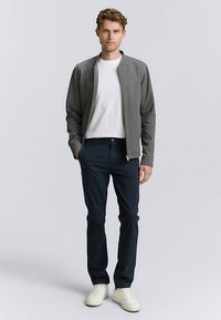 Grijze bomberjack, wit T-shirt, marineblauwe broek en witte sneakers; voorzien van ritssluiting en geribbelde manchetten. Eenvoudige, moderne outfit.