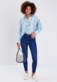 Camicia a maniche lunghe blu a fiori, jeans skinny scuri, sneakers color crema e borsa a tracolla con fantasia. Tessuto liscio con vestibilità rilassata.