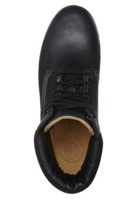 Botín de piel negra hasta el tobillo con puntera redonda, diseño con cordones, puño acolchado y costuras blancas en contraste. El interior presenta un forro en tono marrón claro.