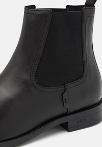 Bottine Chelsea en cuir noir avec panneaux latéraux élastiques, texture lisse, bout arrondi et petit talon carré orné d'un logo discret.