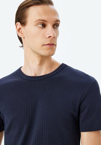 Mørkeblå ribbet t-shirt med rund halsudskæring og korte ærmer, lavet af blødt bomuldsstof, der har en subtil tekstur og en tætsiddende pasform.
